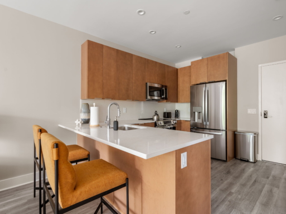 Modern kitchen with tall wooden cabinets, stainless steel appliances, and a white countertop island with bar stools.