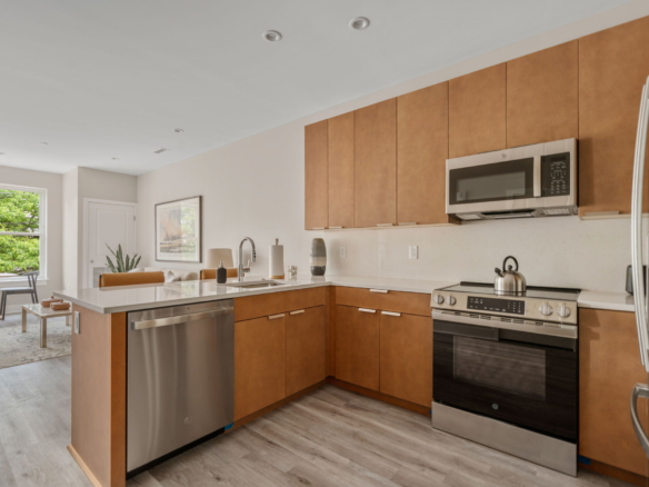 Open-plan kitchen with oak cabinets, stainless steel appliances, and a large island facing a living area in the background.
