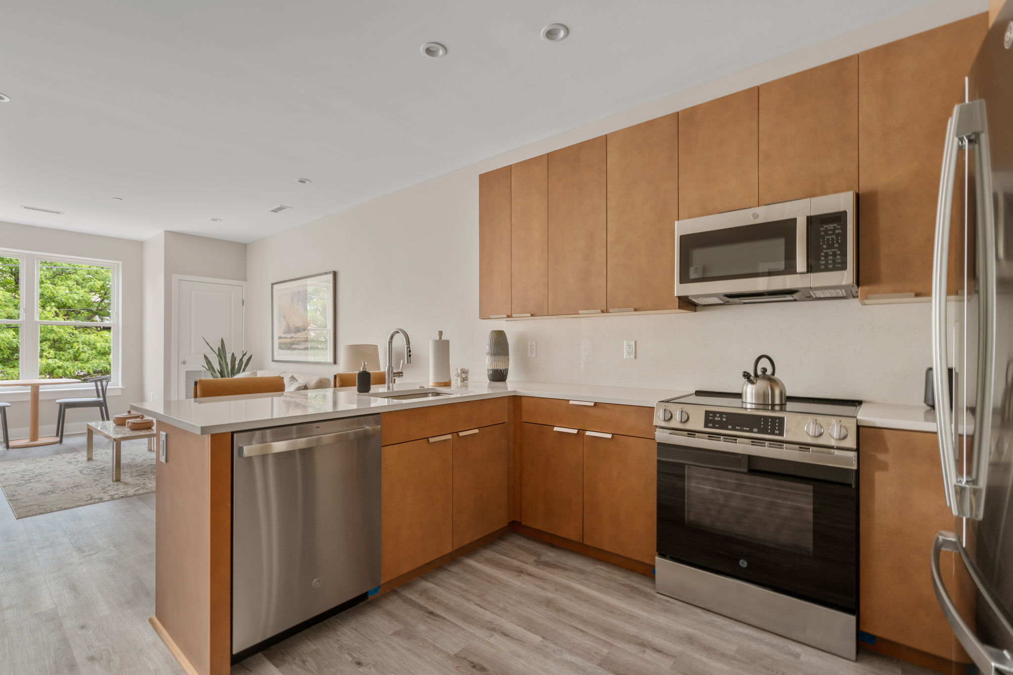 Dexter Street Commons, 1-Bed 2026-06-02 Open-plan kitchen with oak cabinets, stainless steel appliances, and a large island facing a living area in the background.