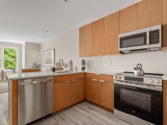Modern kitchen with wooden cabinets, stainless steel appliances, and a marble countertop island with a sink and dishwasher nearby.