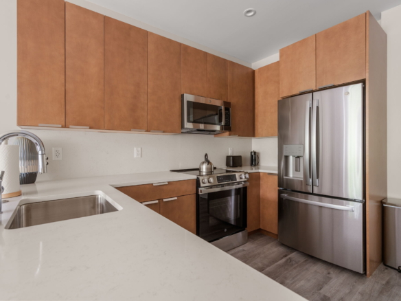 Modern kitchen with tall brown wood cabinets, stainless steel refrigerator, microwave, and gas range along the wall.