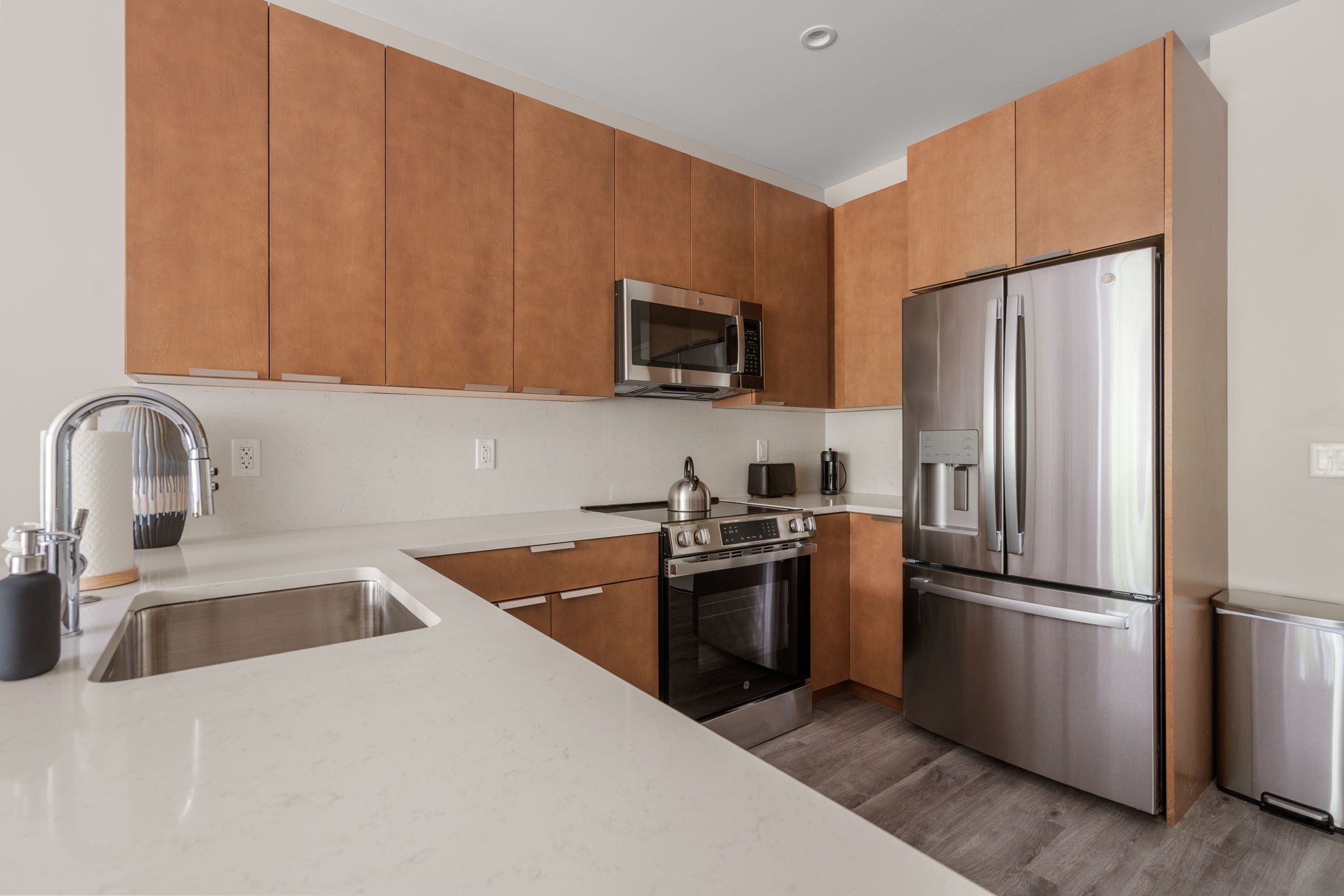 Dexter Street Commons, 1-Bed 2026-06-05 Modern kitchen with tall brown wood cabinets, stainless steel refrigerator, microwave, and gas range along the wall.