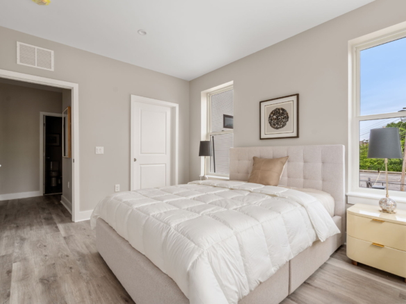 Modern bedroom interior with a beige upholstered bed, white quilt, and tan pillows under soft daylight
