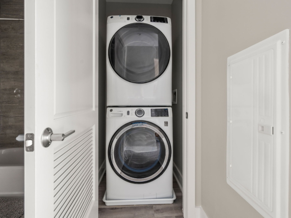 Stacked white front-loading washer and dryer in a laundry closet with doors open.