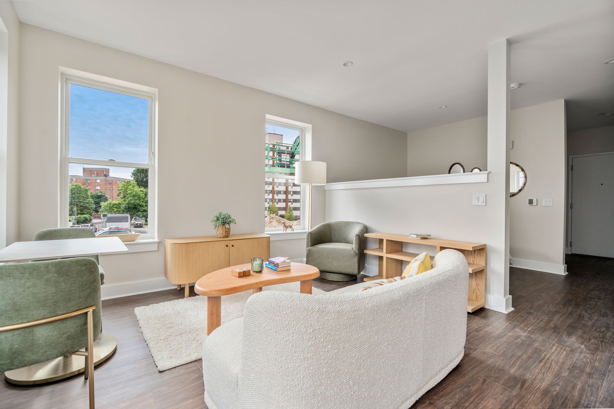 Bright, modern living room with large windows, light walls, and green accent chairs around wooden coffee tables.