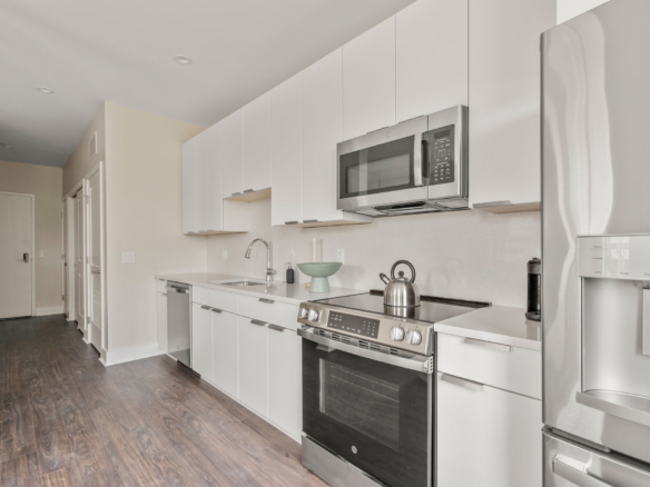 Modern white kitchen with stainless steel microwave and range, glossy cabinets, and a tall refrigerator along the right edge.