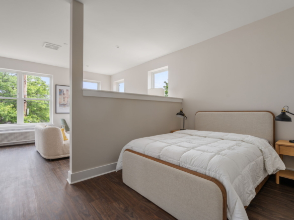 Bright modern bedroom with two twin beds, white quilts, and a partition wall, plus large windows overlooking trees.