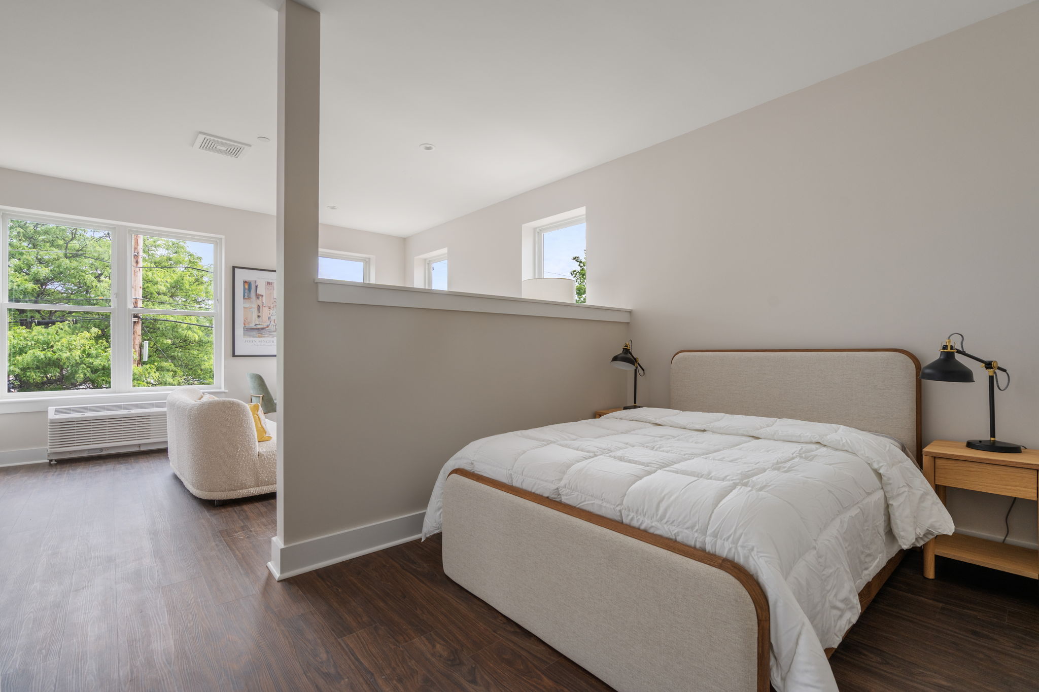 Bright modern bedroom with two twin beds, white quilts, and a partition wall, plus large windows overlooking trees.