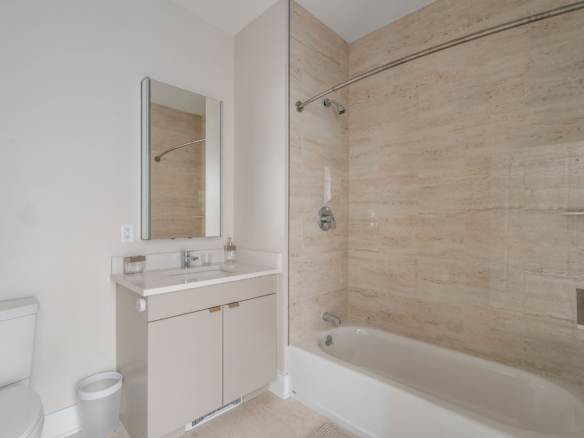 Modern bathroom with white vanity, mirror, and glass-enclosed shower featuring beige tile walls.