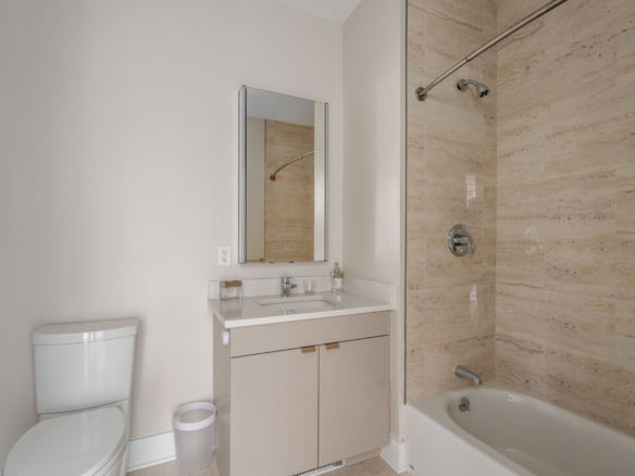 Modern white bathroom with a vanity, sink, and mirror next to a beige tiled shower area