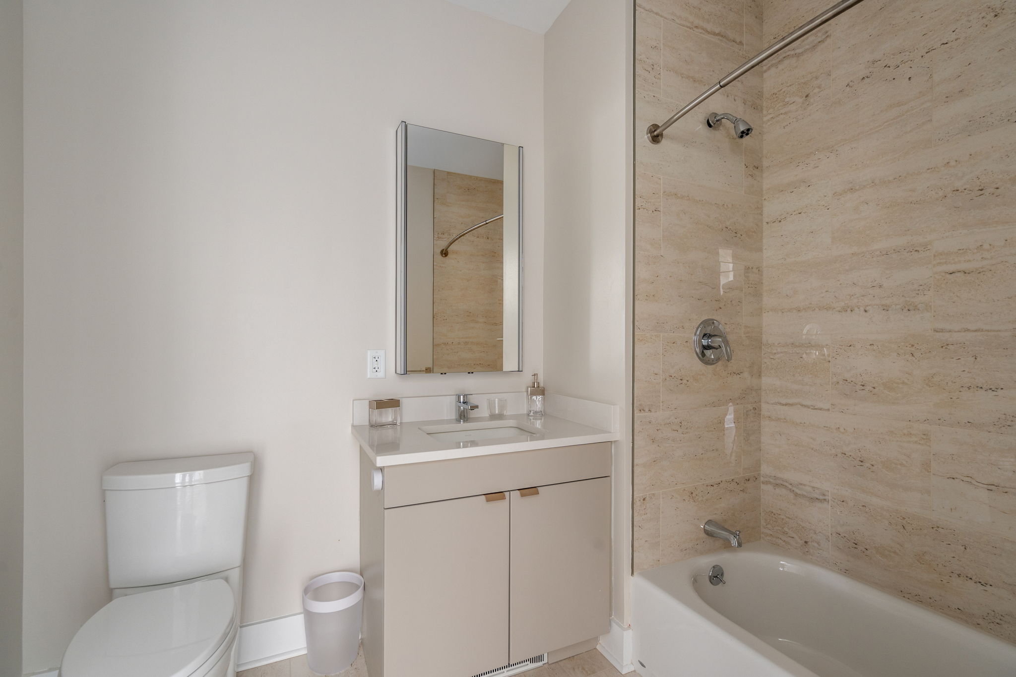 Modern white bathroom with a vanity, sink, and mirror next to a beige tiled shower area