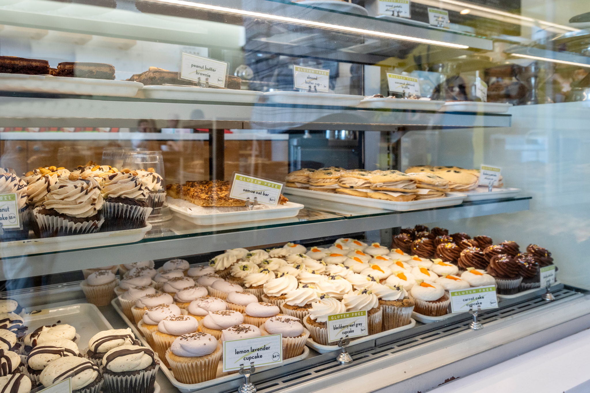 Assorted cupcakes and pastries displayed in a glass bakery case with gluten-free labels visible on signs